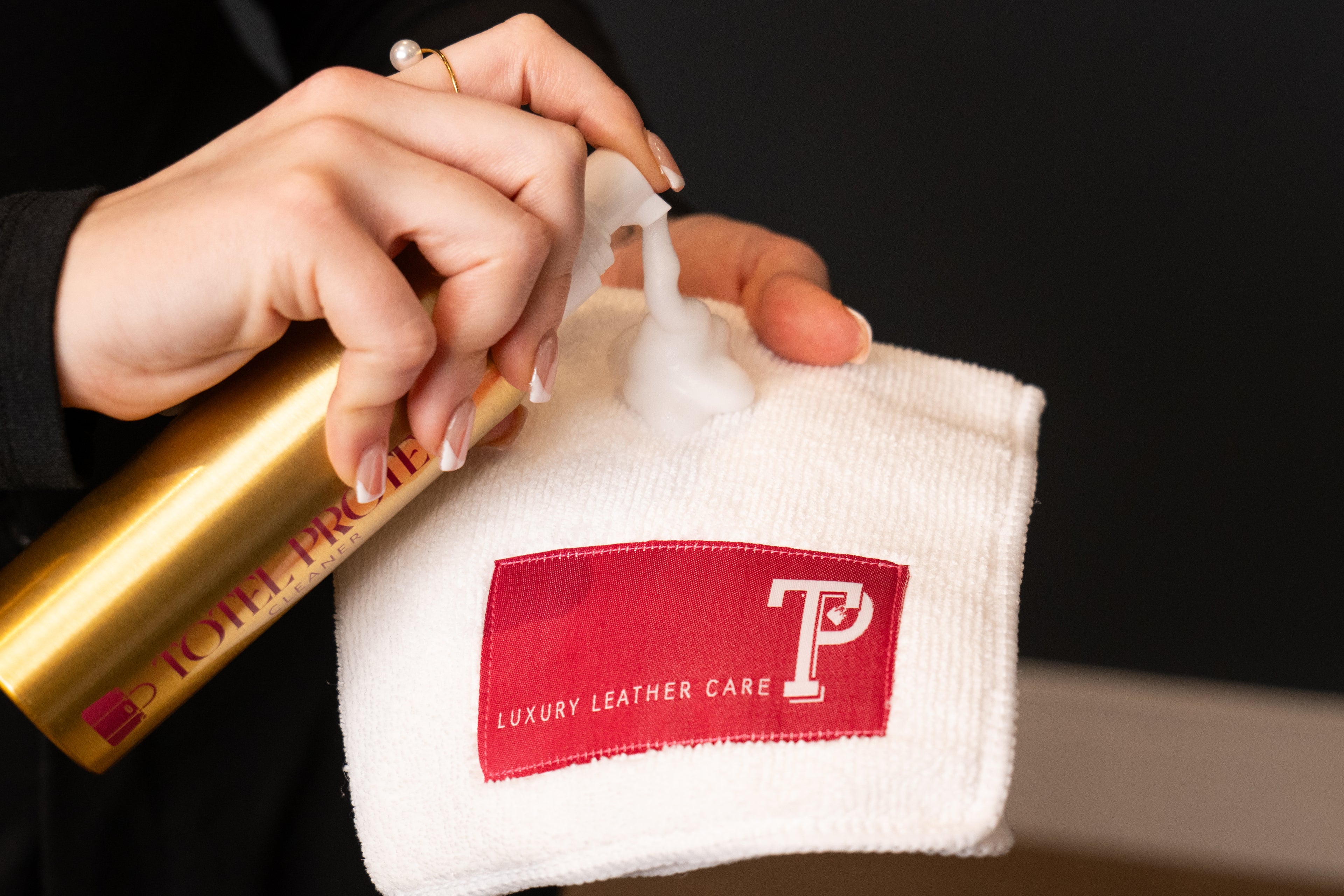 Person holding a gold bottle and white cloth with a red logo, likely for leather care.