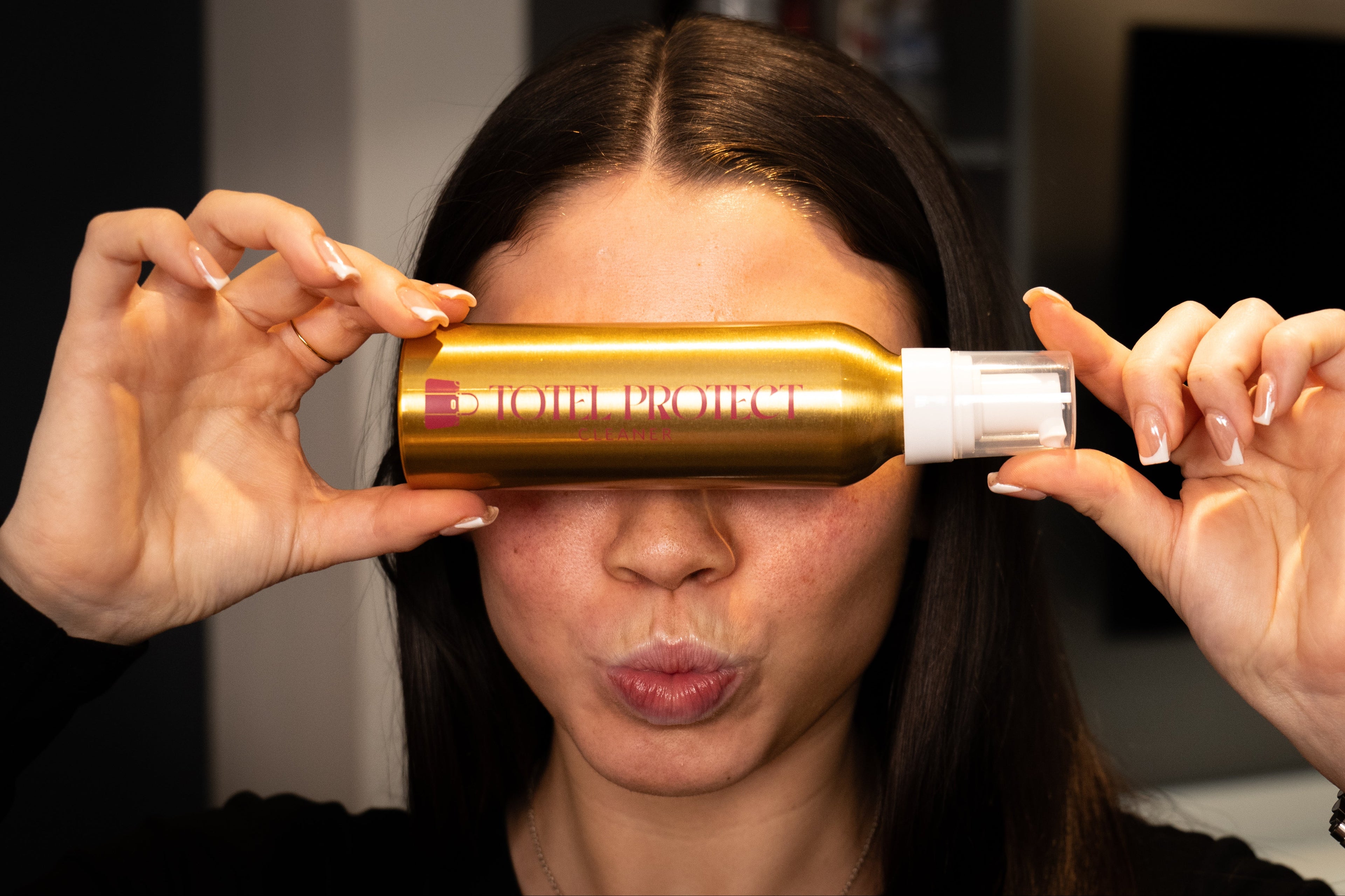 Person holding a gold and white bottle near their face with a blurred background