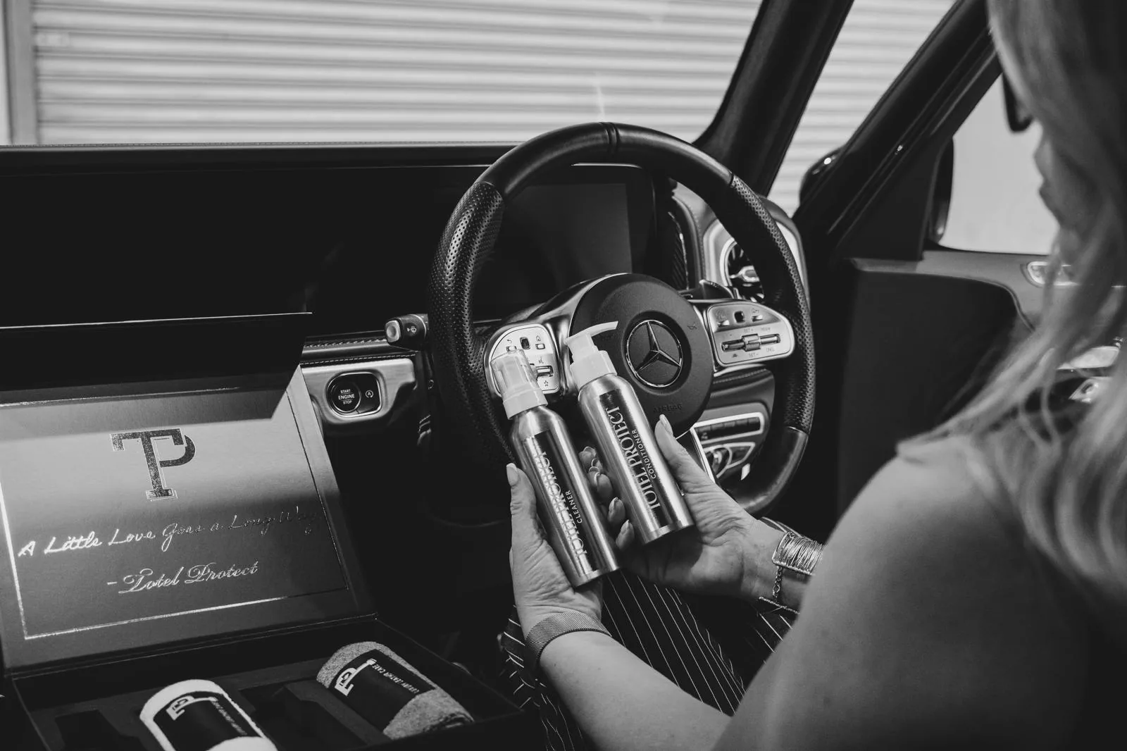 Totel Protect leather cleaner and conditioner held at the wheel of a car, with the open kit on the passenger seat