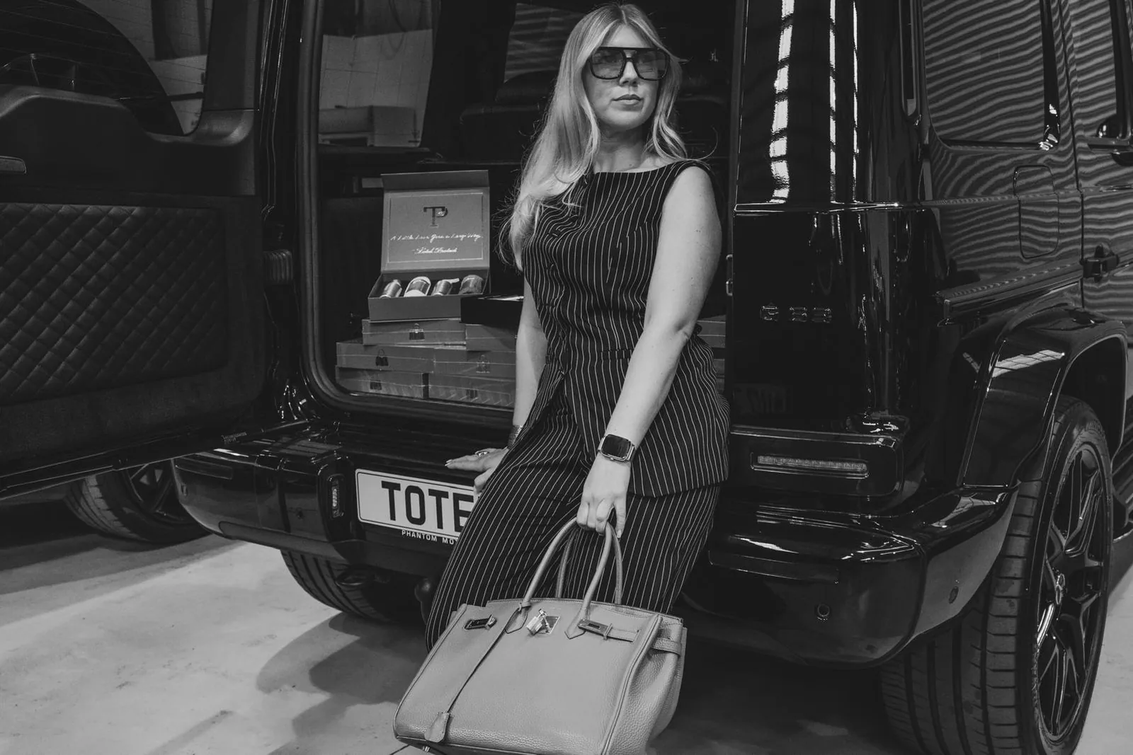 A person in a pinstripe outfit seated at the open boot of a black car, with Totel Protect kits stacked inside